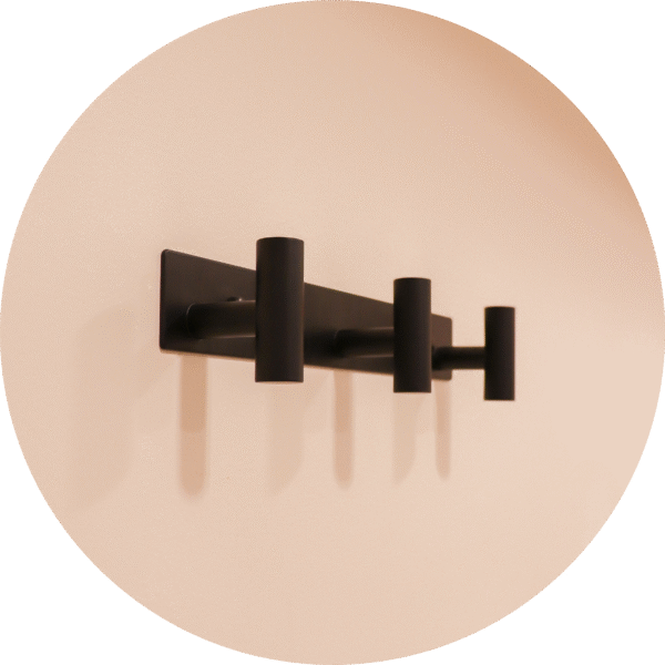 A modern black wall-mounted coat rack with three hooks for hanging coats, capes, and purses.