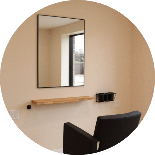 A large black-framed mirror mounted on the wall with a stylist chair beneath it.
