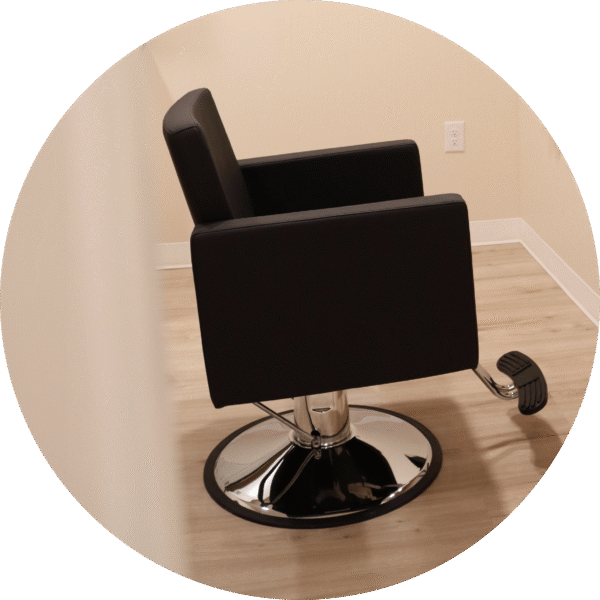 A sleek, black stylist chair with chrome base and footrest.